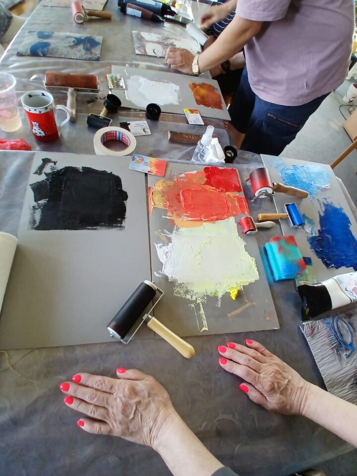 Preparations for printing. Several colours have been rolled onto the plates – orange, black and pale yellow. A paint roller lies next to them.