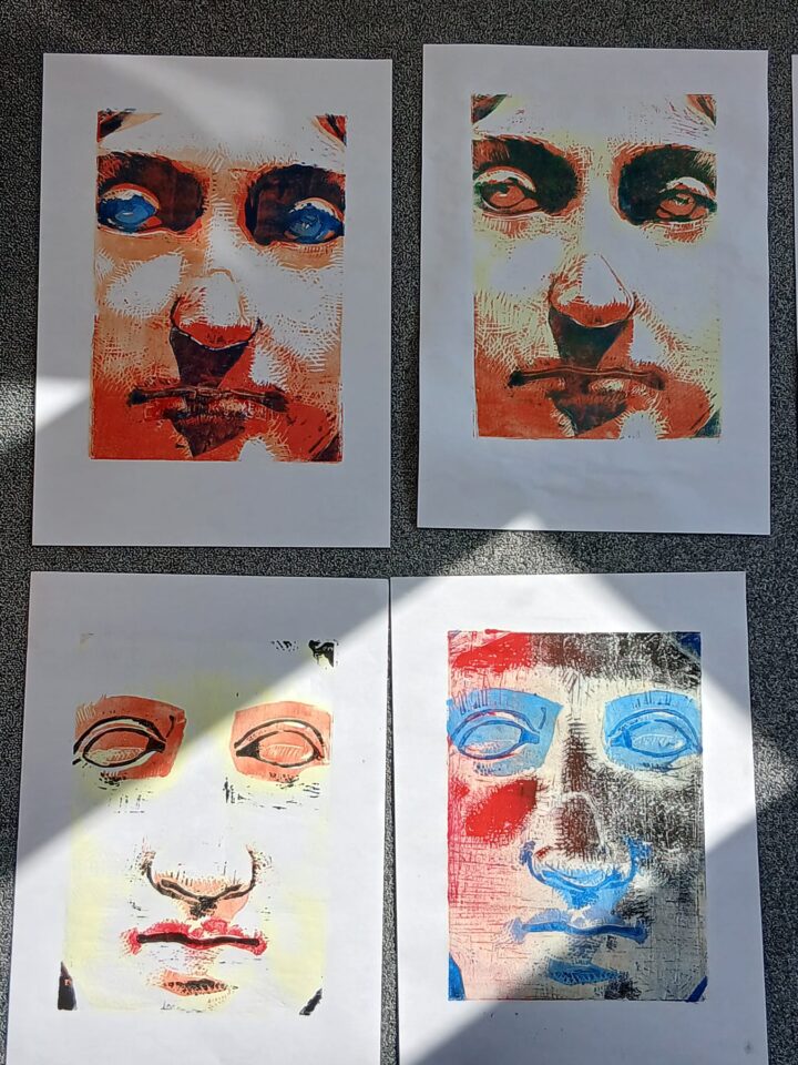 A view of four finished prints. The ancient face appears in a wide variety of colours on white paper.